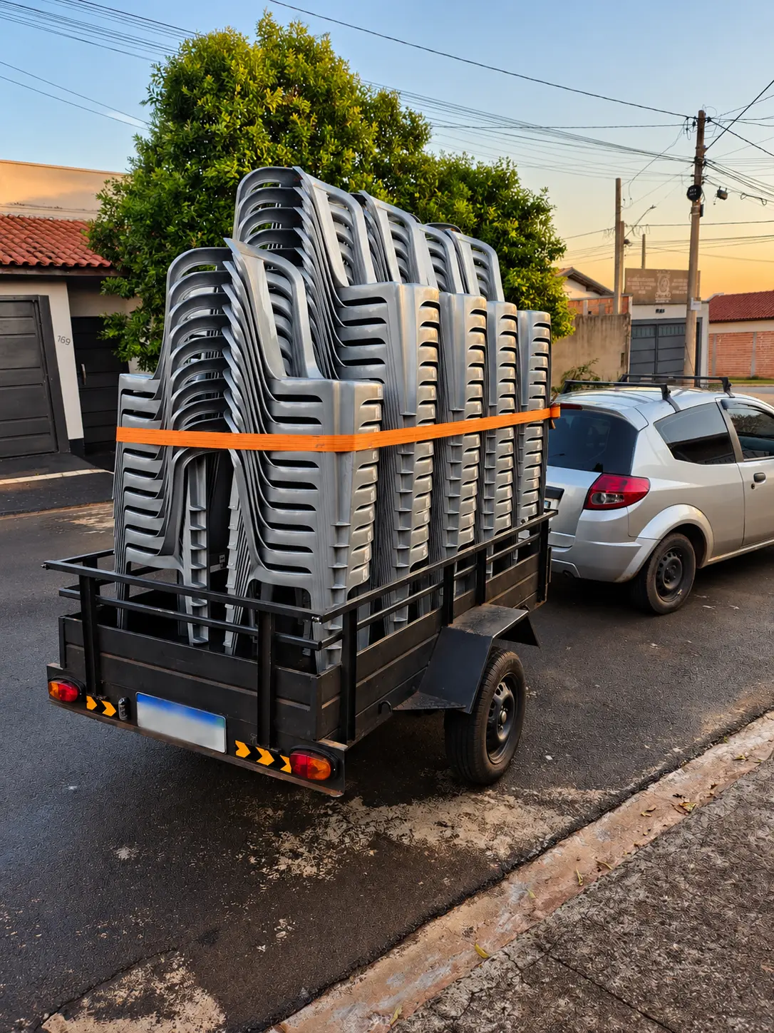 Carro rebocando trailer com cadeiras empilhadas para entrega